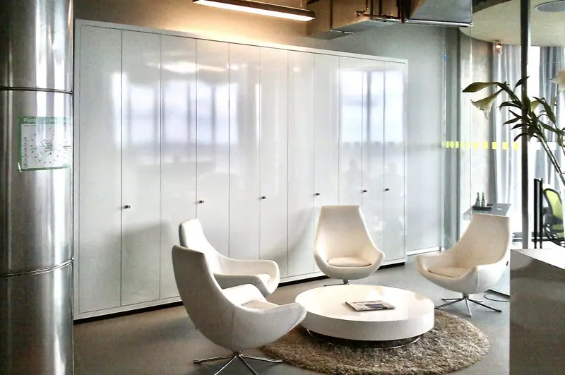 Büro-Lounge mit Sesseln vor einer Wand aus weißen Hochglanz-Schränken