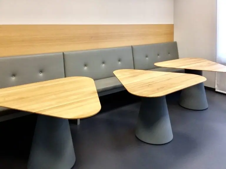 Gepolsterte Sitzbank mit Holzrückwand und drei Tischen mit geschwungener Holzplatte