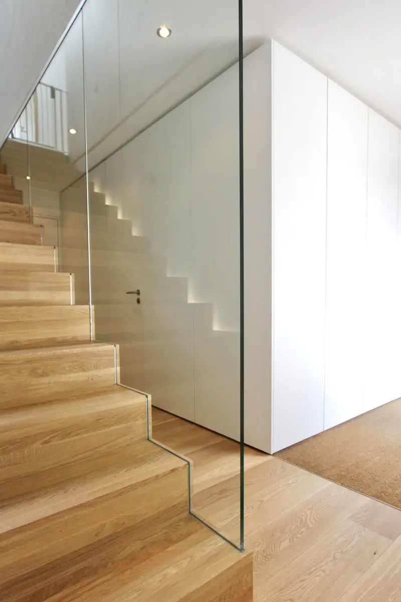 Holztreppe mit Glasgeländer und weißer Wand